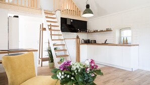 Une cuisine moderne avec des meubles blancs, un escalier en bois et un coin repas agrémenté d’une chaise jaune.