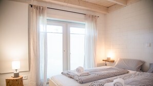 Une chambre avec deux lits, des rideaux blancs, une table de chevet avec une lampe et une petite étagère avec une bougie.