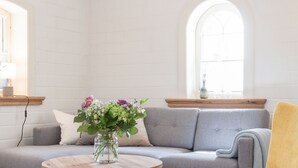 Un salon moderne avec un canapé gris, un fauteuil jaune, une table basse en bois et un vase de fleurs.