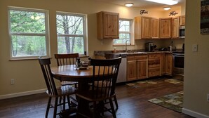 Una cocina con armarios de madera, una mesa de comedor con sillas y ventanas amplias con vistas a árboles.