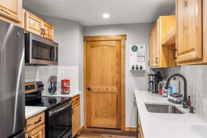 A compact kitchen with wooden cabinets, stainless steel appliances, a white countertop, and a built-in microwave. - SnowPine Condo, Sleeps 8, Patio, A/C (Great Valley)