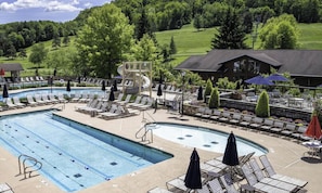 A pool area with lounge chairs, a water slide, and a view of a green landscape.