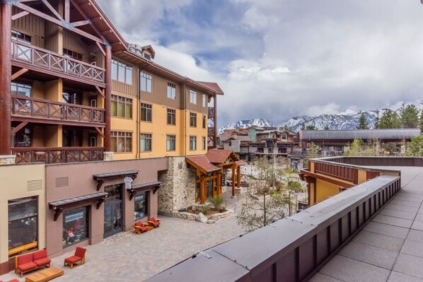 A multi-story hotel with balconies, outdoor seating, and a view of snow-capped mountains. - Village 3211 | Hot Tub and Pool Access (Mammoth Lakes)