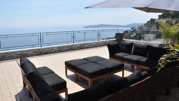 A terrace with outdoor seating, a view of the sea, and a stone wall. - SKYLINE Penthouse Apartment Cap-D'ail, Monaco (Cap-d'Ail)