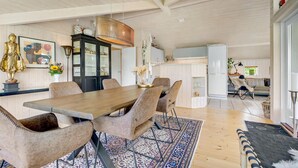 Ett rymligt matområde med ett träbord och stolar, ett svart skåp med glasdörrar och en hängande lampa.