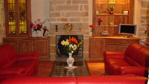A living room with a fireplace, red leather sofas, a television, and wooden shelves with decorative items. - The Closerie du Manoir for 7 people (Audierne)