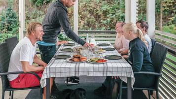 Un área de comedor al aire libre con mantel a cuadros, rodeada de sillas, y una persona sirviendo comida.