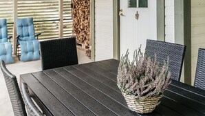 A dining area with a dark wooden table and wicker chairs, a wicker basket with flowers, and a view of a covered patio with blue chairs and a wooden wall. - Vacation home B by Interhome (Porvoo)
