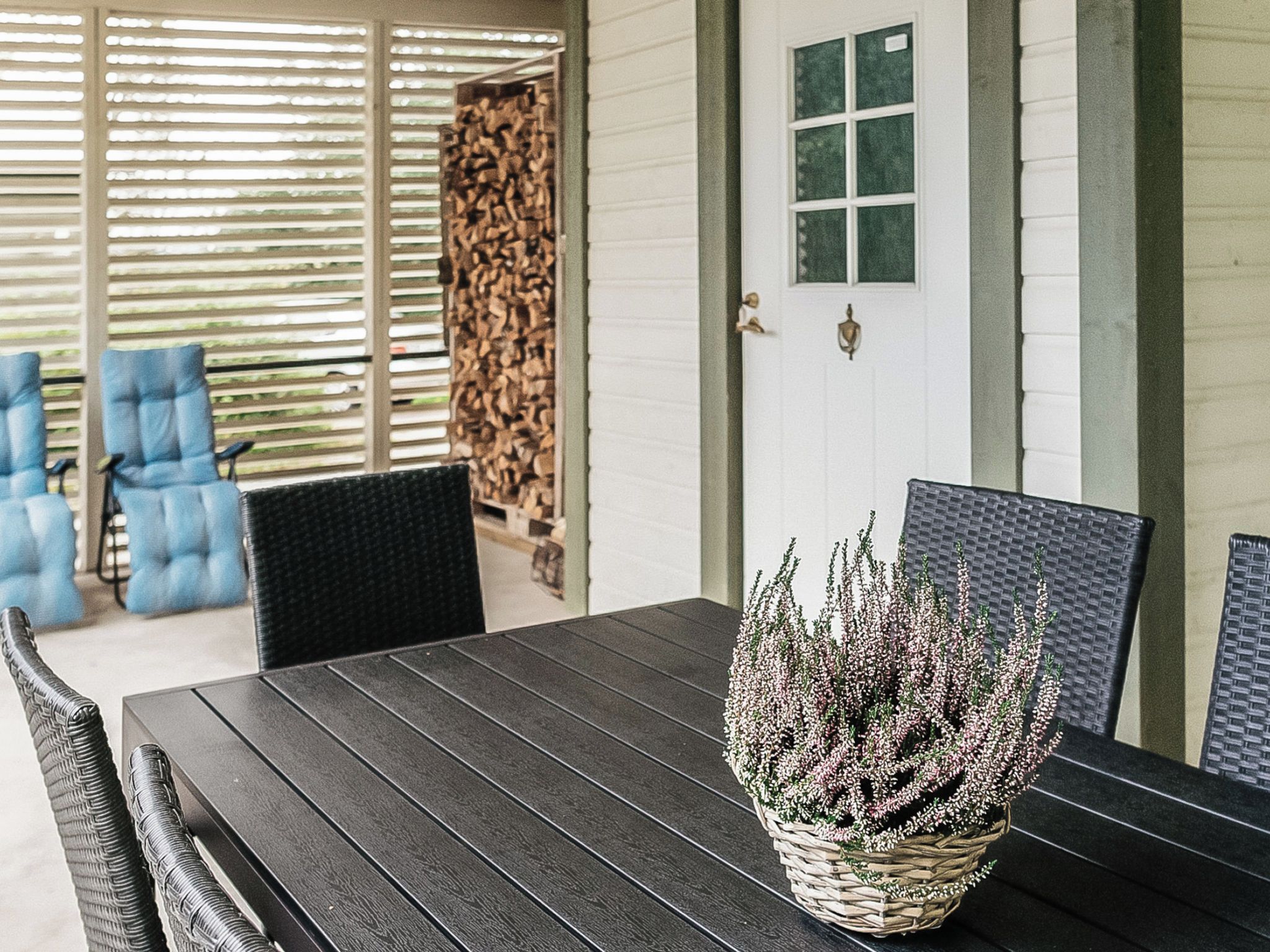 A dining area with a dark wooden table, wicker chairs, and a basket of flowers.