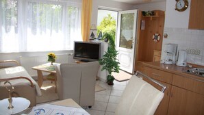Ett väl upplyst rum med en tv, ett matbord, en stol, en liten växt och en köksdel med en kaffebryggare.
