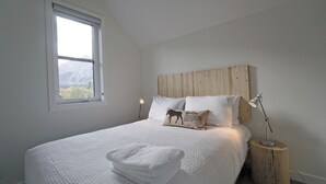 Un dormitorio con una cama grande, un cabecero de madera, una ventana con vistas a las montañas y una lámpara de noche.