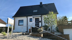 A two-story house with a dark tiled roof, a front door, and a small garden area with gravel and plants. - Vacation apartment T & T 3 (Malente)