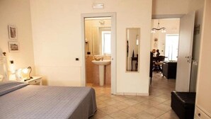 A bedroom with a bed, a nightstand, a dresser, and a bathroom visible through an open door.