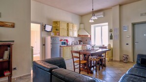 A compact kitchen with a dining area, a black leather sofa, and a bookshelf.