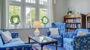 Una sala de estar con sofás de flores azules, una mesa de centro de vidrio y una estantería llena de libros.