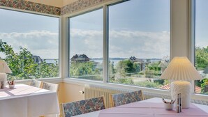 Un comedor con ventanas amplias, una mesa cubierta con mantel rosa y vistas a casas y follaje.
