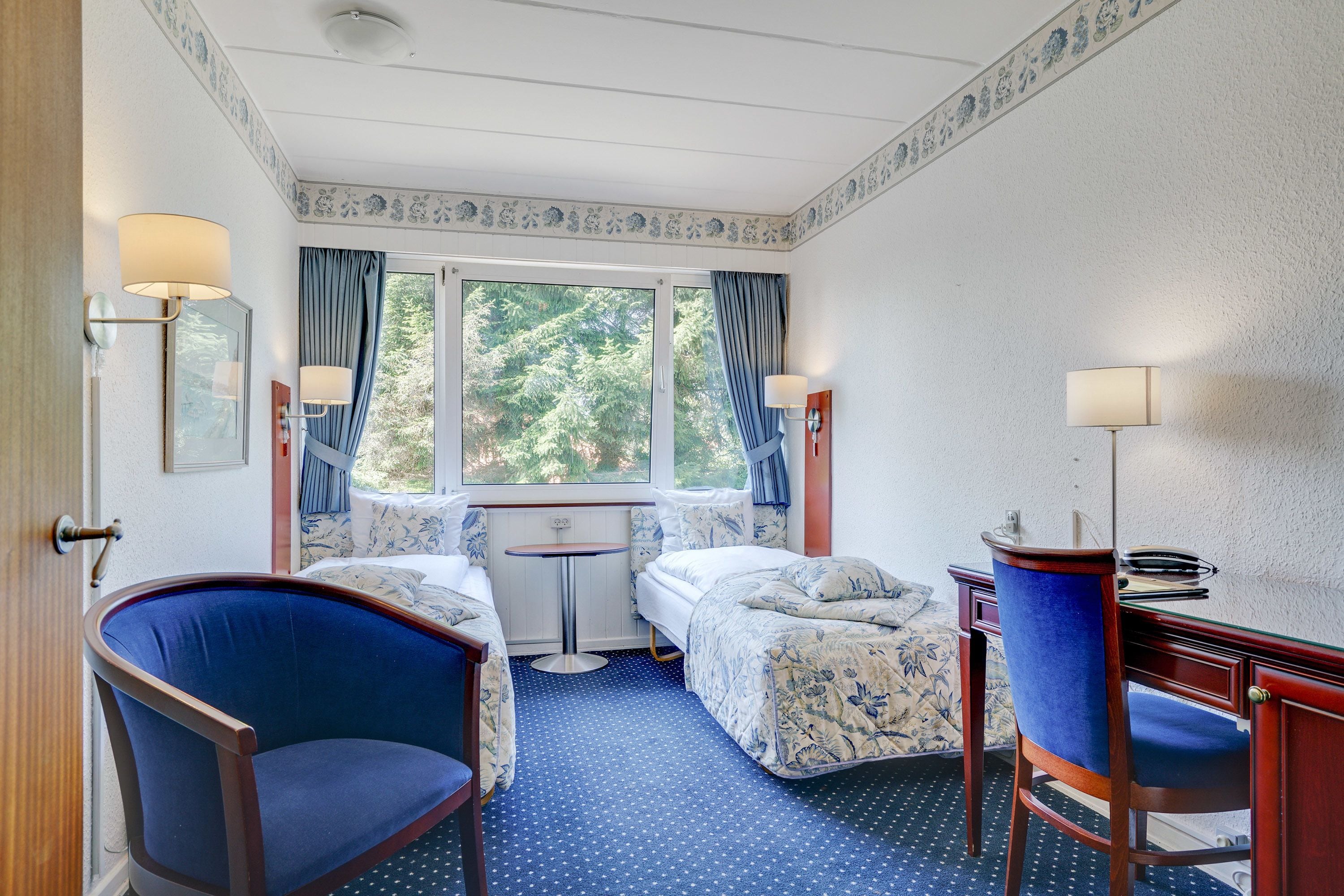 A hotel room with a bed, a desk, a chair, and a window with curtains.