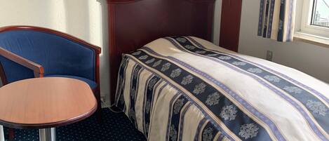 Una habitación de hotel con cama, una mesa redonda, una silla y un ventanal con cortinas.