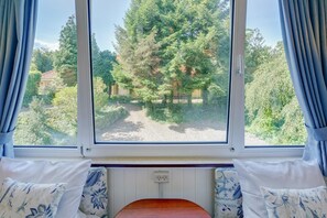 Una habitación con un ventanal grande, una cama con almohadones estampados y vistas a una zona boscosa.