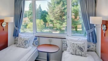 Ein Zimmer mit zwei Betten, einem kleinen Tisch und einem Fenster mit Vorhängen.