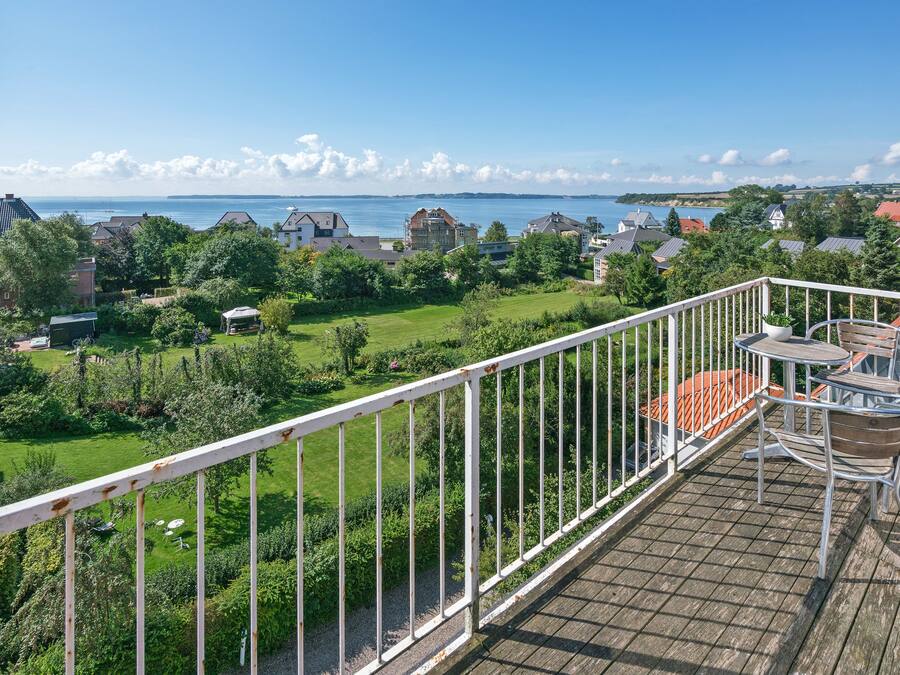 A balcony with a view of a residential area, a grassy lawn, and a body of water in the distance.