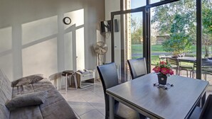 A modern living room with a sofa, a dining table with chairs, a TV, and a fan. There is a large window providing a view of the outdoors. - Modern chalet 4-6 ppl, pets allowed, private terrace (Veauchette)