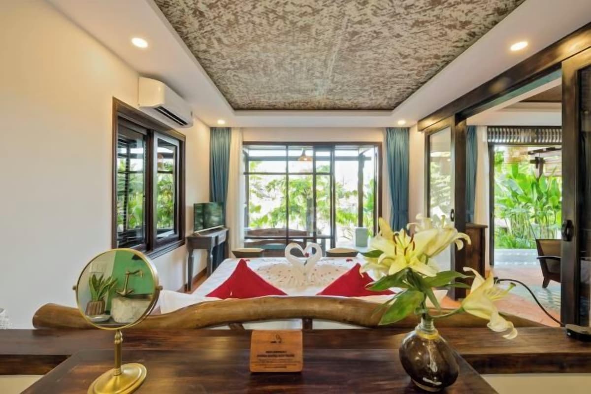A hotel lobby with a reception desk, a large window with a view of greenery, and a modern ceiling design.