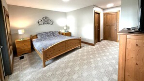 A bedroom with a wooden bed, bedside tables, a wall-mounted light fixture, and a wooden wardrobe. - Luxury Lakefront Townhouse 3Bed,3Bath Pool•Hot Tub•Beach - Canada's warmest lake (Osoyoos)