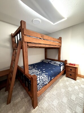 A bunk bed with a ladder, a bedside table with drawers, and a patterned bedspread.