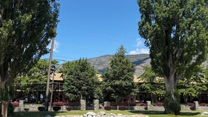 A building with a stone facade, a paved area with a stone wall, and a view of mountains in the background. - Luxury Lakefront Townhouse 3Bed,3Bath Pool•Hot Tub•Beach - Canada's warmest lake (Osoyoos)