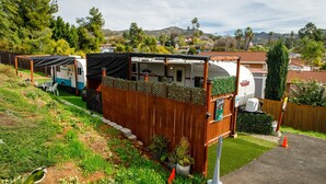 A recreational vehicle (RV) parked in a backyard with a wooden fence, surrounded by potted plants and a small garden. - End of summer fun in Bettie Blue! (El Cajon)