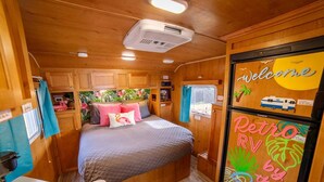 A cozy RV interior with a bed, a sink, and a refrigerator displaying a welcome message. - End of summer fun in Bettie Blue! (El Cajon)