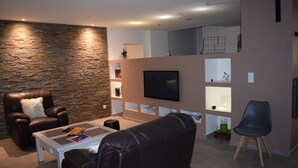 A modern living room with a stone wall, leather chairs, a flat-screen TV, and built-in shelves.