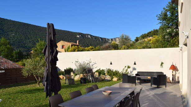 An outdoor patio with a dining table and chairs, surrounded by a white wall and a mountain backdrop.
