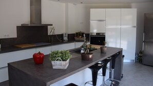 A modern kitchen with white cabinets, a stainless steel range hood, and a central island with bar stools.