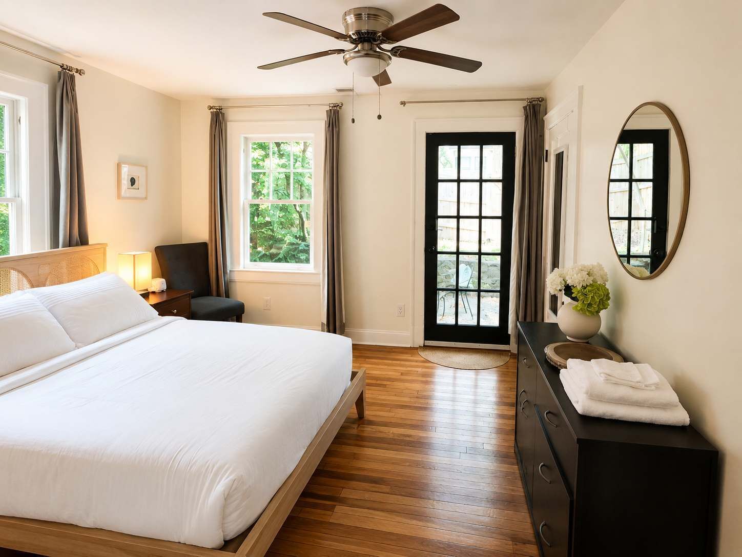 Habitación de hotel con cama, escritorio, silla, ventilador de techo, puerta con vistas y espejo en la pared.