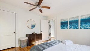 A bedroom with a bed, a ceiling fan, a washing machine, and artwork on the wall. - Chic Craftsman, Walk Downtown (Durham)