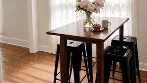 A dining area with a wooden table, black stools, a vase with flowers, and a clock on the wall.