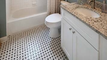 Un baño con una bañera blanca, inodoro, lavabo con encimera de granito y cortina de ducha.