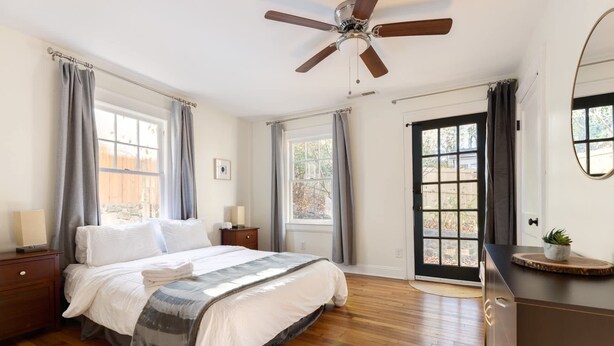 A bedroom with a bed, wooden floor, ceiling fan, windows, and a dresser. - Chic Craftsman, Walk Downtown (Durham)