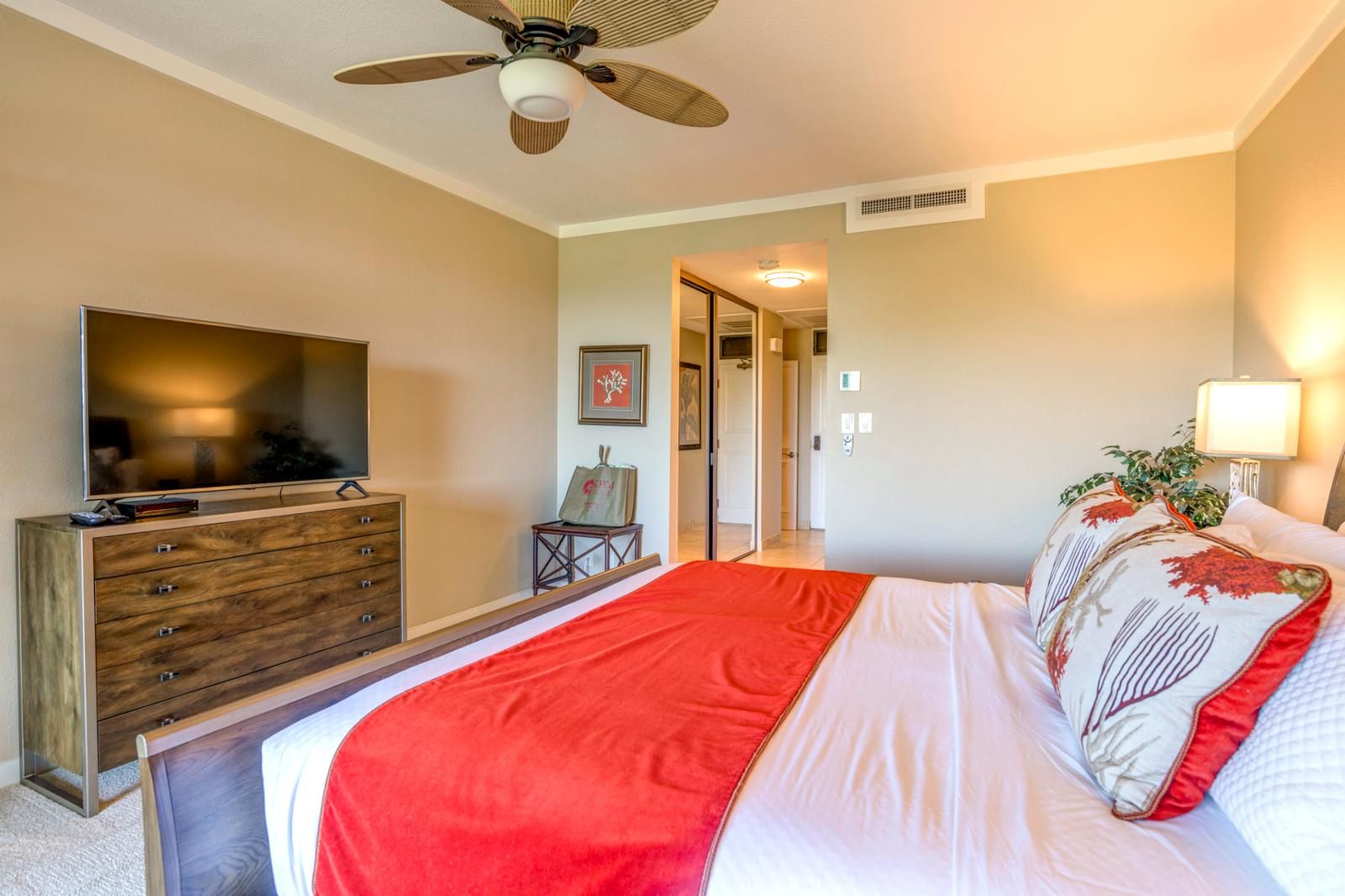 Ein Schlafzimmer mit Bett, Fernseher, Kommode und Deckenventilator.