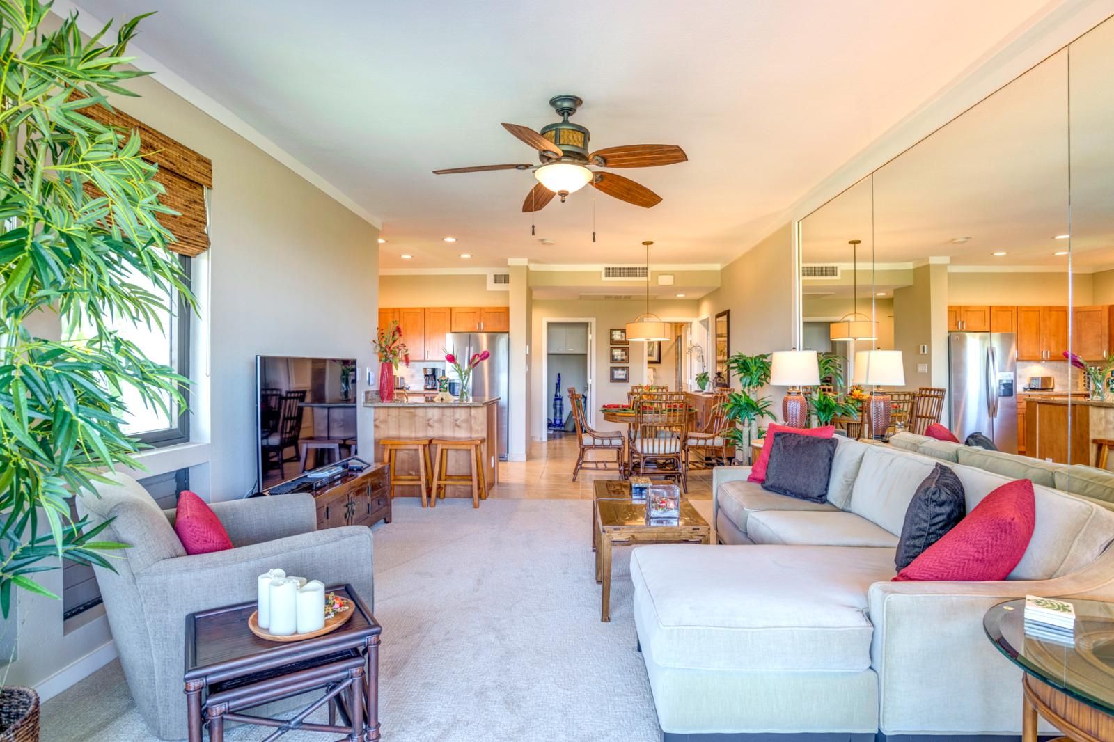 A spacious living room with a sofa, coffee table, and a television. There is a kitchen area with wooden cabinets and a dining table.