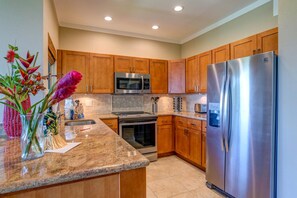 A kitchen with wooden cabinets, stainless steel appliances, a granite countertop, and a vase with flowers. - Kapalua Golf Villas | Ocean View 1 BR | Car Incl. w/ 6+ Nights | KGV-16T4 by KBM (Lahaina)