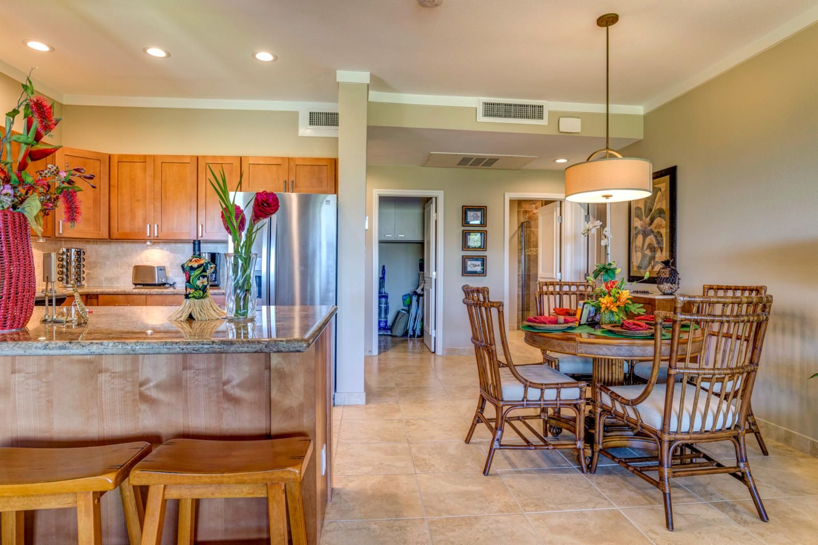 A modern kitchen with wooden cabinets, a stainless steel refrigerator, and a central island with a vase of flowers.