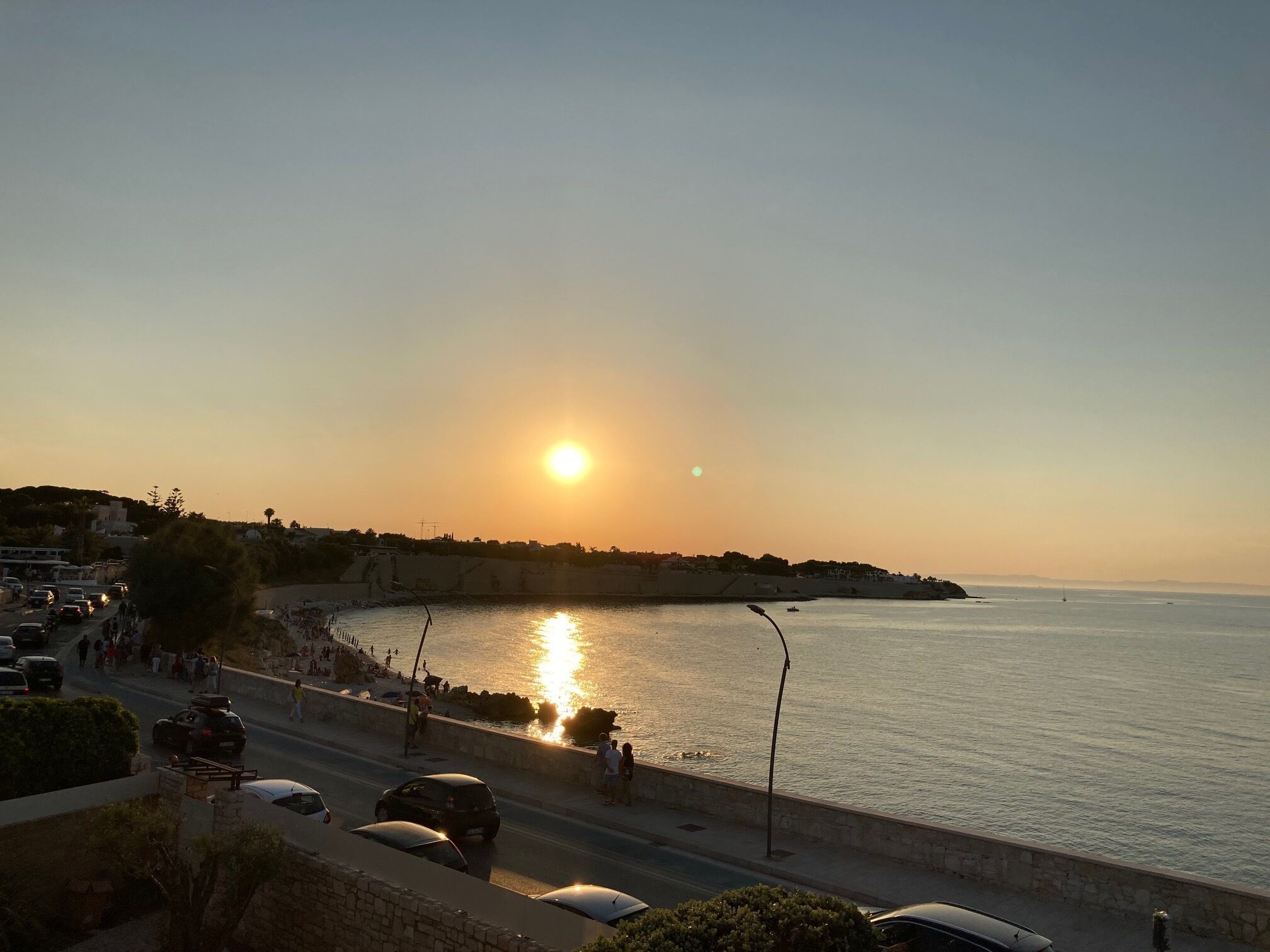 Une route côtière offrant une vue sur le coucher de soleil, une plage et un ciel dégagé.