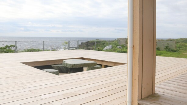 Eine Holzdielen-Terrasse mit Sitzgelegenheit aus Stein mit Blick auf das Meer.