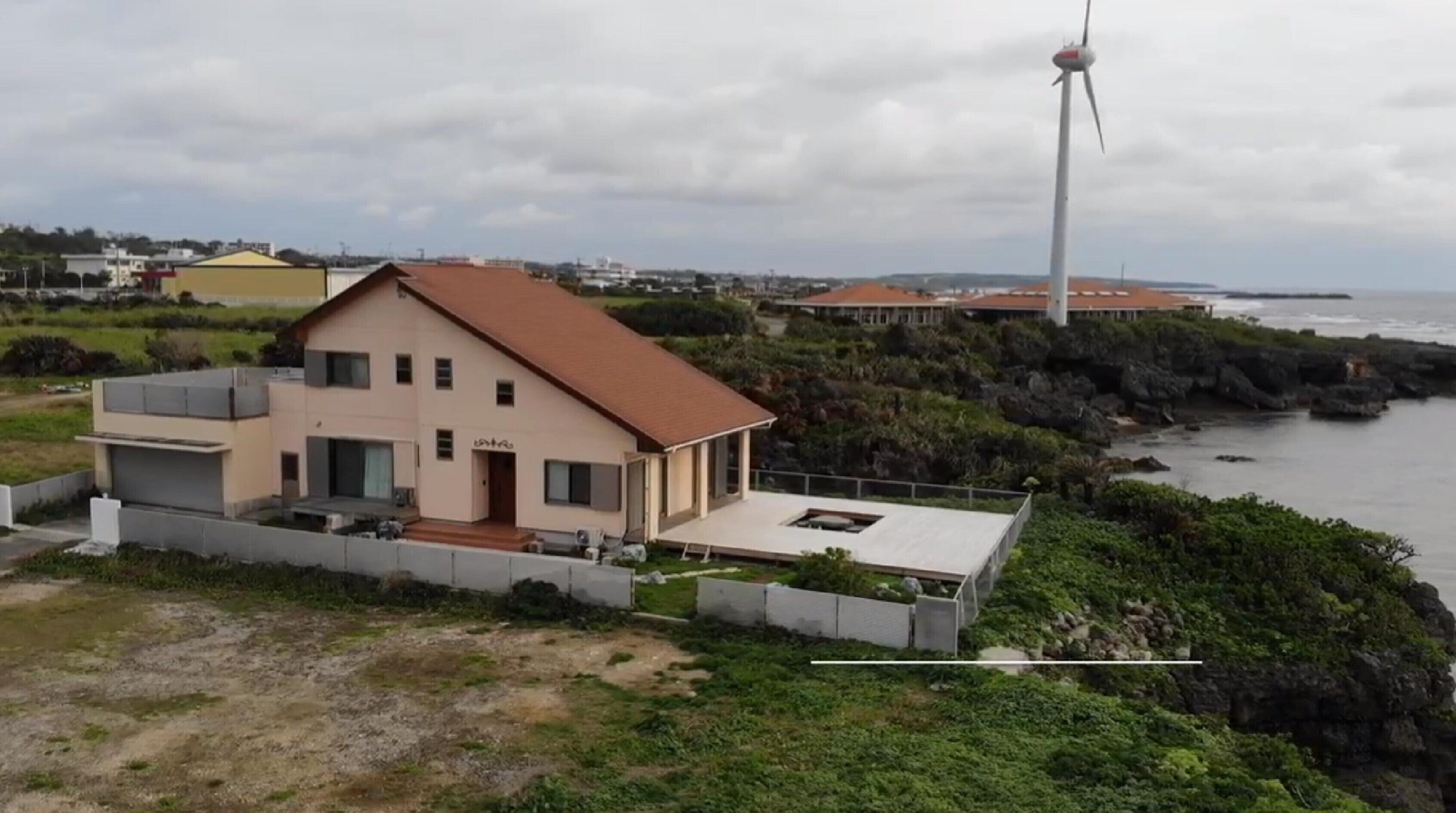 A coastal house with a wind turbine in the background.