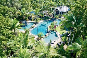 Vista aérea de um resort com uma piscina central rodeada por vegetação exuberante e palmeiras.