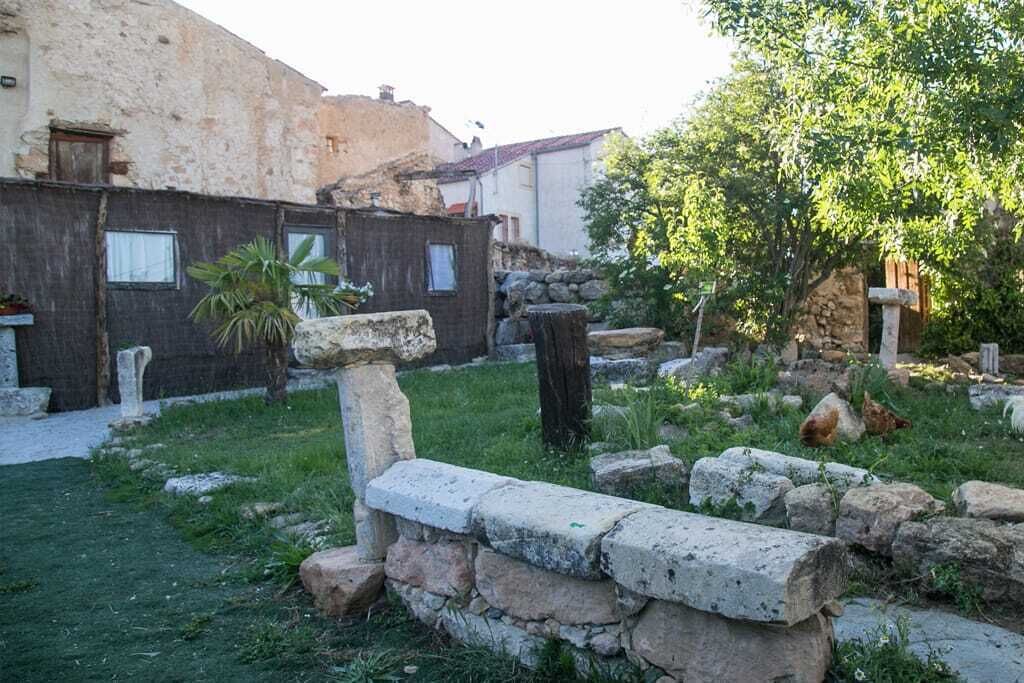 Une cour bordée de murs en pierre, avec un palmier et des poulets.