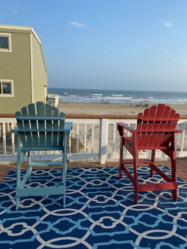 A deck with two Adirondack chairs facing a beach.